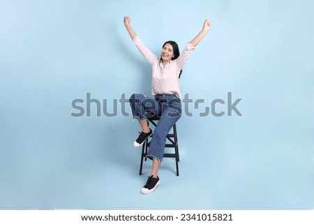 The Asian woman in casual clothes sit on the chair in the blue background.