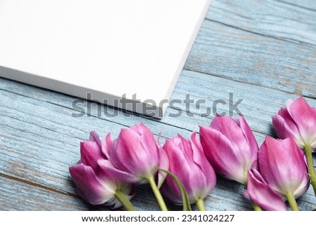 Blank white canvas mockup with flowers on blue wood background. Mockup with white canvas on wood, corner closeup