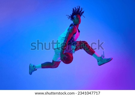 Slam dunk Ambitious young man, basketball player in minions, playing basketball against gradient blue background in neon lights. Concept of professional sport, competition, hobby, competition, ad