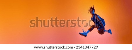 Athletic young man, basketball player in motion, jumping with ball against orange background in neon lights. Concept of professional sport, competition, hobby, competition. Banner. Copy space for ad