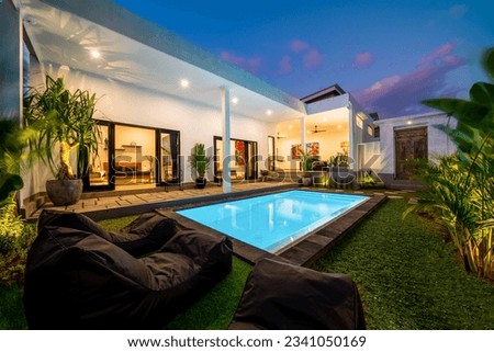 Tropical villa view with garden, swimming pool and open living room at sunset.