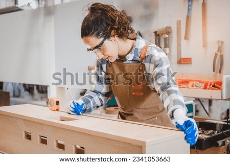 Portrait of a female carpenter using a pencil to mark a piece of wood during work in a furniture factory. Concept. Hobby designer of young start-ups and SME small businesses. Royalty-Free Stock Photo #2341053663
