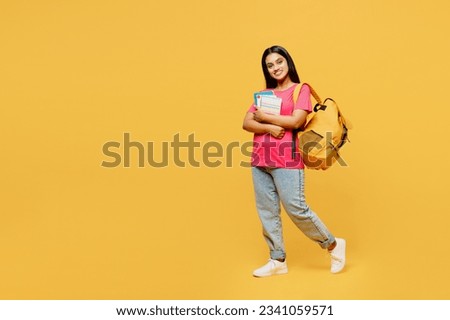 Full body young happy teen Indian girl student she wear casual clothes backpack bag hold books look camera isolated on plain yellow background studio portrait. High school university college concept