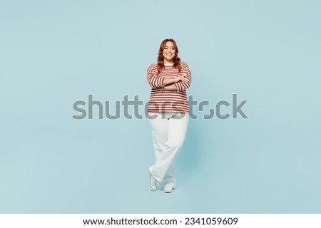 Full body smiling fun happy young chubby overweight woman wearing striped red shirt casual clothes hold hands crossed folded isolated on plain pastel blue background studio portrait. Lifestyle concept