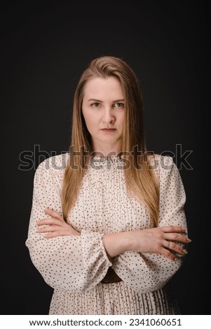 Young serious woman with crossed arms isolated on black wall with copy space. Beautiful girl with folded hands looking at camera. Closeup portrait of lady in dress looks confident on black background. Royalty-Free Stock Photo #2341060651