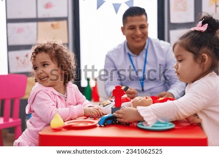 Hispanic man and girls playing supermarket game sitting on table at kindergarten