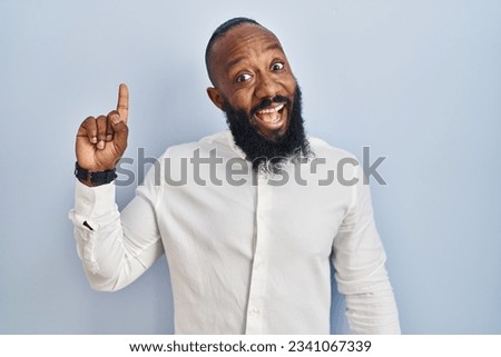 African american man standing over blue background pointing finger up with successful idea. exited and happy. number one. 