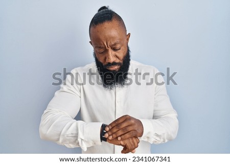 African american man standing over blue background checking the time on wrist watch, relaxed and confident  Royalty-Free Stock Photo #2341067341