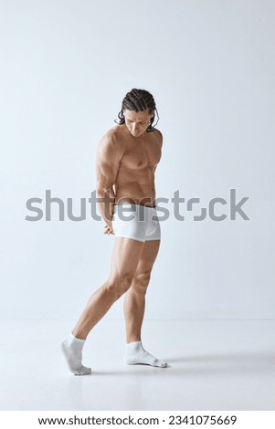 Full-length portrait of handsome mature man with muscular strong body standing shirtless in boxers against grey background. Concept of men's beauty, body care, sport, wellness, healthy lifestyle, ad Royalty-Free Stock Photo #2341075669