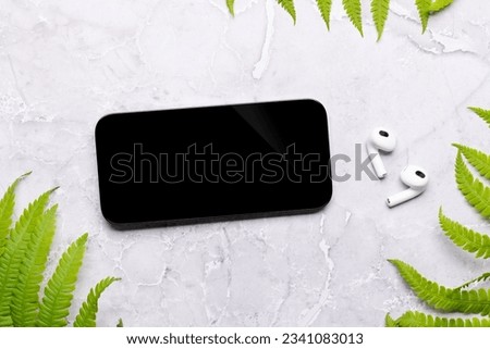 Smartphone with blank screen on a table surrounded by green nature leaves, perfect design mockup