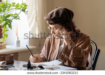 Thoughtful freelancer designer sitting at creative table draw illustration for order. Involved artist young woman in stylish eco clothes creates ink drawings. Art hobby with therapy for mental health