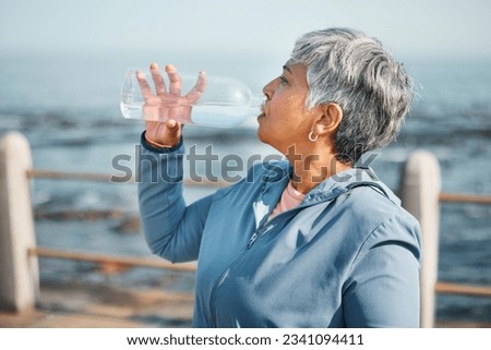 Outdoor, fitness or senior woman drinking water for hydration, wellness and thirsty on beach run, training or exercise. Bottle, runner or elderly person refresh with cold liquid on retirement workout Royalty-Free Stock Photo #2341094411