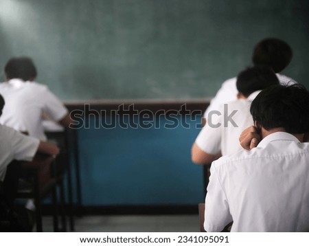 Students reading exam answer sheets exercises in classroom of school with headache
and stress