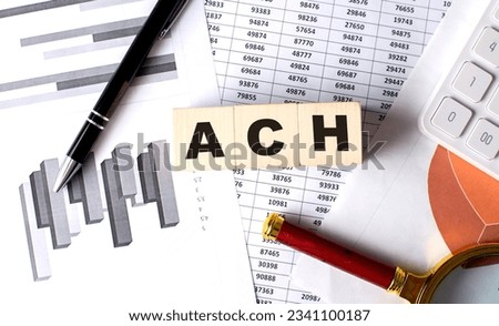 ACH Automated Clearing House text on a wooden block on graph background with pen and magnifier Royalty-Free Stock Photo #2341100187