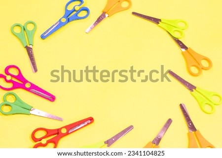 Colorful children's scissors isolated on yellow background. Small scissors arranged in a circle. Back to school idea concept. Different design. Top view photo. Copy space, blank, empty area. No people