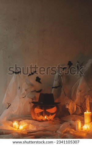 Spooky Jack o lantern carved pumpkin, spider web, ghost, bats and glowing light in dark. Scary atmospheric halloween party decorations, space for text. Happy Halloween! Trick or treat