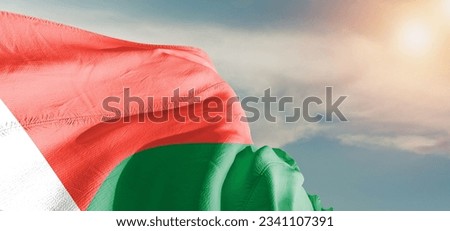 Madagascar national flag cloth fabric waving on beautiful sky Background.
