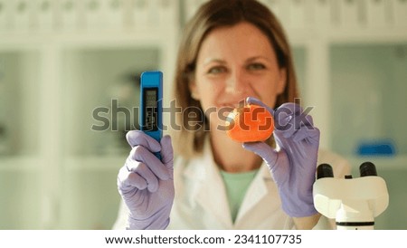 Scientist woman holds in hands tangerine and tester for measuring amount of nitrates in chemical laboratory