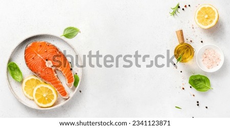 Fresh raw salmon steaks with spices, lemons and pink salt on white plate. Top view of fish with copy space. Keto recipe. Royalty-Free Stock Photo #2341123871