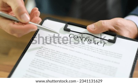 Businessman is holding tablet in hand and pointing with pen at contract documents