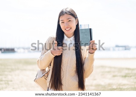 Young Chinese woman holding a passport at outdoors with thumbs up because something good has happened