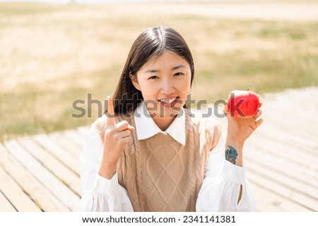 Young Chinese woman with an apple at outdoors pointing up a great idea