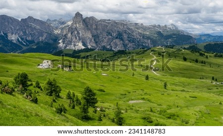 Dolomite mountain range landscape scenery in summer with grassy plains and a ruins structure, some trees, and a hiking trail before craggy peaks during cloudy weather in italy. Royalty-Free Stock Photo #2341148783