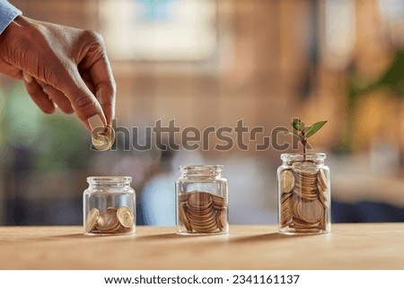 Close up of black woman hand adding money in coin in a jar. Girl hand holding coin adding money in glass jar of different sizes. Investment, savings and interest concept. Royalty-Free Stock Photo #2341161137