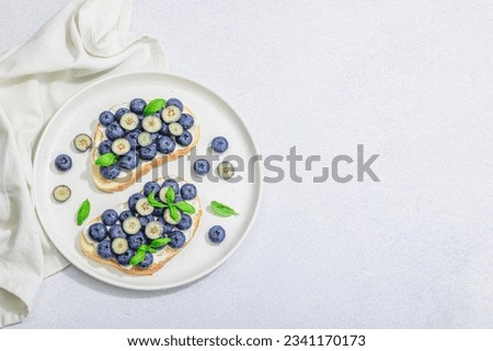 Fresh bread sandwiches with sweet blueberries, cream cheese and basil leaves. Good morning breakfast concept. Hard light, dark shadow, white stone concrete background, top view Royalty-Free Stock Photo #2341170173