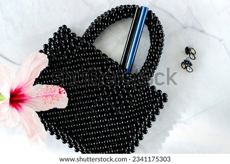 Eyeliner in elegant beads handmade bag on marble background. Make-up products concept. Fashionable and Elegant cosmetic products. Creative beauty products photography. Natural flower.