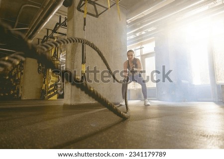 Muscular fitness woman trains triceps with two cables by her hands on background of fitness center Royalty-Free Stock Photo #2341179789