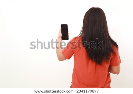 Back view of young woman standing while holding a cell phone. Isolated on white