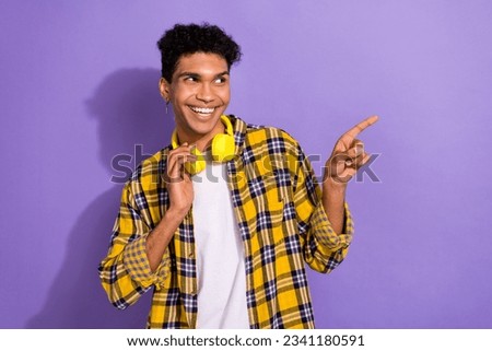 Photo of dreamy thoughtful guy wear plaid yellow shirt earphones pointing finger looking empty space isolated violet color background