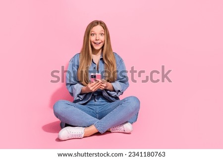 Photo of astonished cheerful girl wear trendy clothes sit floor buy iphone rejoice purchase empty space isolated on pink color background