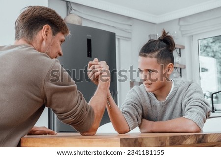 Father competing in arm wrestling with teen son, family spending time together.  Royalty-Free Stock Photo #2341181155