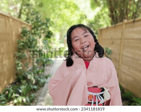 Asian girl in pink kimono smiling in Japanese garden