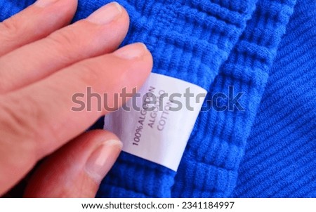 White laundry label tag with sign , 100 percent algodon cotton on a blue fabric texture.Selective focus.