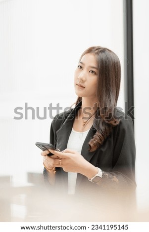 Beautiful successful asian businesswoman holding mobile phone using smartphone in office chatting with business mannequin 