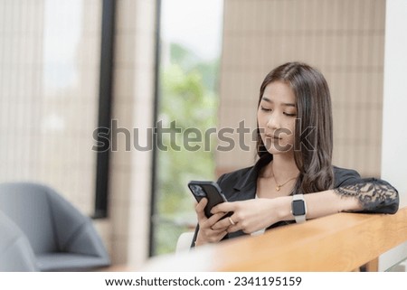 Beautiful successful asian businesswoman holding mobile phone using smartphone in office chatting with business mannequin 