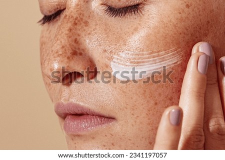 Close-up of female face with freckled skin. High-detailed shot of woman skin applying moisturizer. Royalty-Free Stock Photo #2341197057