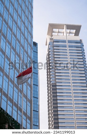 Indonesian flag in front of a modern office building.  The flag of Indonesia is a simple bicolor with two equal horizontal bands, red (top) and white (bottom), symbolize courage and holiness