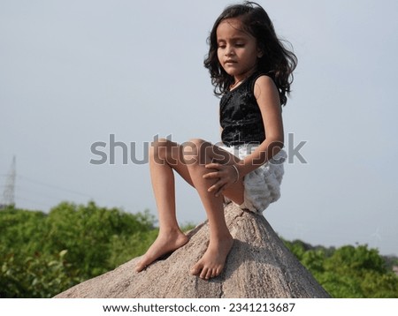 Little girl sitting on hill and walking around it. Cute and nice light present filter effect on portrait camera photo. Clear subject focus behind defocus background. Kid wearing black and white dress.