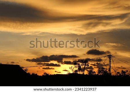 The orange sky is filled with clouds with silhouettes of trees