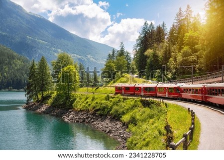 Red train moving along lake in beautiful mountain landscape in Switzerland Royalty-Free Stock Photo #2341228705