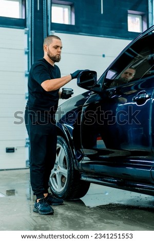 Focused Male car wash worker in black gloves polishes the mirror of a luxury blue car using polishing sponge car care concept