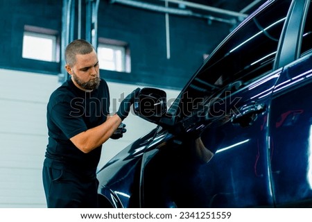 Focused Male car wash worker in black gloves polishes the mirror of a luxury blue car using polishing sponge car care concept