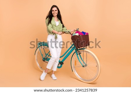 Full length photo of pleasant satisfied nice woman wear green shirt white pants stand near bicycle isolated on beige color background Royalty-Free Stock Photo #2341257839