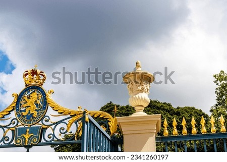 Golden coat of arms of the Dutch royal family on the fence of Noordeinde palace against dark clouds, The Hague, The Netherlands, Europe