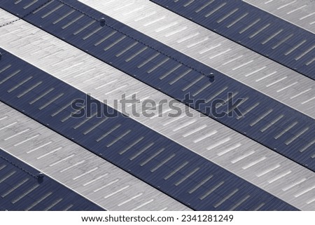 An aerial view taken from a helicopter of the roof of a large industrial building. The huge roof of he warehouse has an abstract striped blue pattern