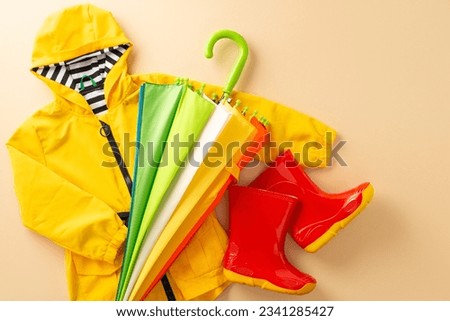 Protective attire for children in rainy weather. Frame top view picture exhibiting colorful gum boots, a raincoat, and an umbrella on a beige isolated background, inviting text or advert incorporation
